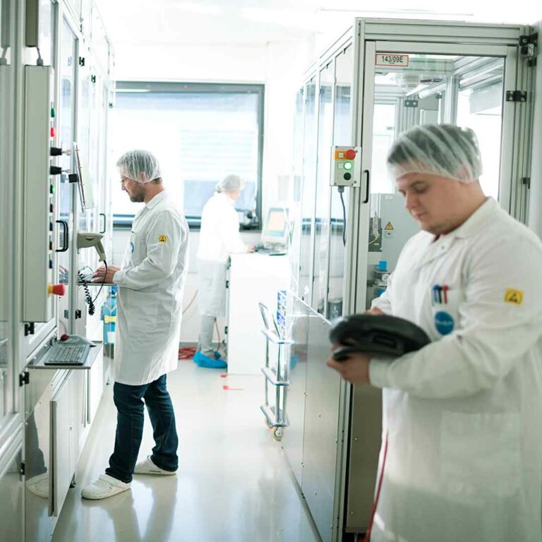 This picture shows two colleagues, in a clean room environment with white coats and hairnet.