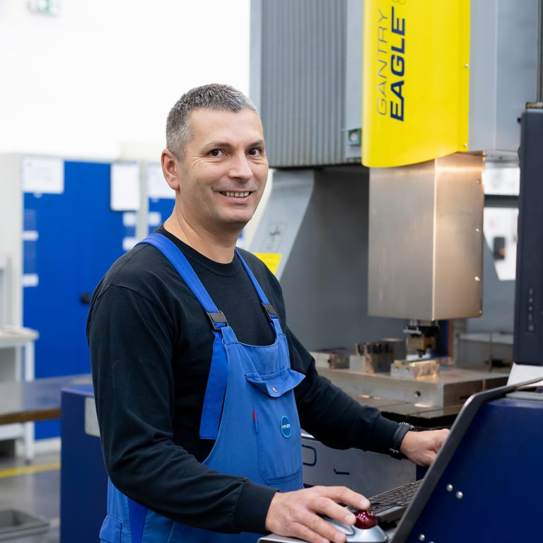The picture shows a colleague in the tool shop standing in front of a machine.